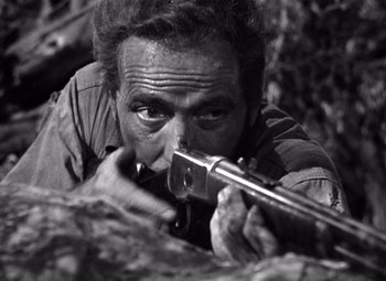 Movie still from “The Treasure of the Sierra Madre” (1948), directed by John Huston – A black - and - white photo of a man holding a rifle; Close Up shot, Low angle