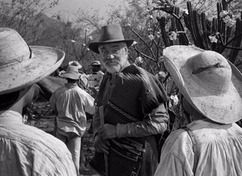 Movie still from “The Treasure of the Sierra Madre” (1948), directed by John Huston – An old man in a hat and a group of people; Medium shot, Over the shoulder angle