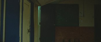 Movie still from “The Vast of Night” (2019), directed by Andrew Patterson – A door open to a dark room with graffiti on the wall; Wide shot, High angle