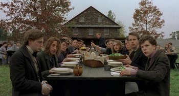 Movie still from “The Village” (2004), directed by M. Night Shyamalan – A group of people sitting at a table with plates of food on it; Wide shot, High angle