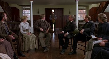 Movie still from “The Village” (2004), directed by M. Night Shyamalan – A group of people sitting in chairs in a living room; Wide shot, Over the shoulder angle