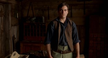 Movie still from “The Village” (2004), directed by M. Night Shyamalan – A man standing in front of a wooden table; Medium shot, Low angle
