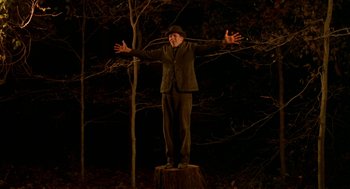 Movie still from “The Village” (2004), directed by M. Night Shyamalan – A man standing on top of a tree stump in the dark; Wide shot, Low angle
