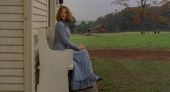 Movie still from “The Village” (2004), directed by M. Night Shyamalan – A woman sitting on a bench in front of a house; Wide shot, Low angle