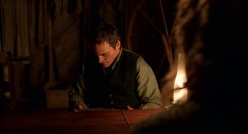 Movie still from “The Village” (2004), directed by M. Night Shyamalan – A man sitting at a table looking down at his cell phone; Medium shot, Over the shoulder angle