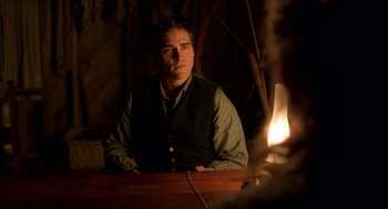 Movie still from “The Village” (2004), directed by M. Night Shyamalan – A man sitting at a table in front of a lit candle; Medium shot, Over the shoulder angle
