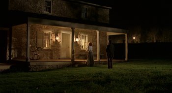 Movie still from “The Village” (2004), directed by M. Night Shyamalan – Two people standing in front of a house at night; Extreme Wide shot, High angle