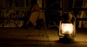 Movie still from “The Village” (2004), directed by M. Night Shyamalan – A person sitting on a bench in the dark; Wide shot, High angle