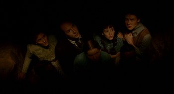 Movie still from “The Village” (2004), directed by M. Night Shyamalan – A group of people standing in a dark room; Medium shot, Overhead angle