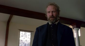 Movie still from “The Village” (2004), directed by M. Night Shyamalan – A man with a beard wearing a suit and tie; Close Up shot, Low angle
