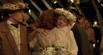 Movie still from “The Village” (2004), directed by M. Night Shyamalan – Two people hugging each other while holding a bouquet of flowers in front of them; Medium shot, Over the shoulder angle