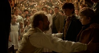 Movie still from “The Village” (2004), directed by M. Night Shyamalan – A man and a boy in front of a group of people; Medium shot, Over the shoulder angle