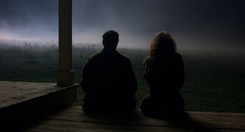 Movie still from “The Village” (2004), directed by M. Night Shyamalan – A man and a woman sitting on a porch looking out at a field; Wide shot, Over the shoulder angle
