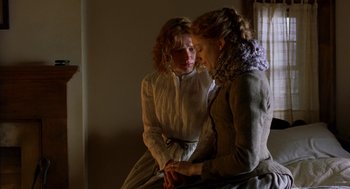 Movie still from “The Village” (2004), directed by M. Night Shyamalan – Two young women sitting in a room , one of whom is holding her hands; Medium shot, Over the shoulder angle