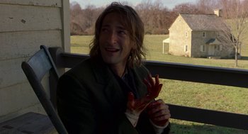 Movie still from “The Village” (2004), directed by M. Night Shyamalan – A man sitting on top of a chair holding a piece of food; Medium shot, Over the shoulder angle