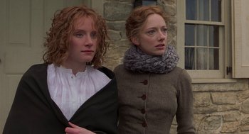 Movie still from “The Village” (2004), directed by M. Night Shyamalan – Two women standing next to each other in front of a stone building; Close Up shot, Low angle