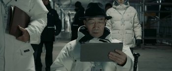 Movie still from “The Wandering Earth II” (2023), directed by Frant Gwo – An older man wearing a black hat looking at a computer screen; Medium shot, Over the shoulder angle
