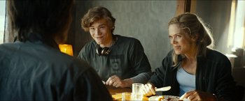 Movie still from “The Wave” (2015), directed by Roar Uthaug – A young man sitting at a dinner table with two other young men; Medium shot, Over the shoulder angle