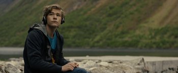 Movie still from “The Wave” (2015), directed by Roar Uthaug – A man sitting on the ground wearing headphones; Medium shot, Low angle