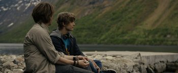 Movie still from “The Wave” (2015), directed by Roar Uthaug – Two young men sitting on the ground near a body of water; Medium shot, Over the shoulder angle