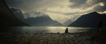 Movie still from “The Wave” (2015), directed by Roar Uthaug – A person sitting on the shore of a body of water; Extreme Wide shot, High angle