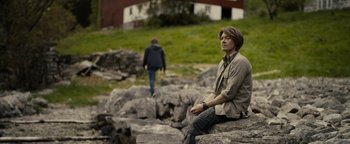 Movie still from “The Wave” (2015), directed by Roar Uthaug – A man sitting on top of a large rock; Medium shot, Over the shoulder angle