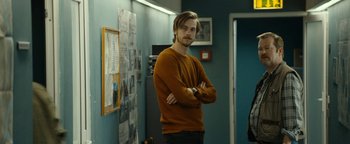 Movie still from “The Wave” (2015), directed by Roar Uthaug – A man standing with his arms crossed in a room; Medium shot, Over the shoulder angle