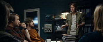 Movie still from “The Wave” (2015), directed by Roar Uthaug – Two men sitting at a table in front of a stack of papers; Medium shot, Over the shoulder angle