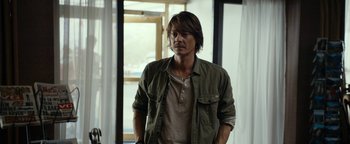 Movie still from “The Wave” (2015), directed by Roar Uthaug – A man standing in front of a window with his hands in his pockets; Medium shot, Over the shoulder angle