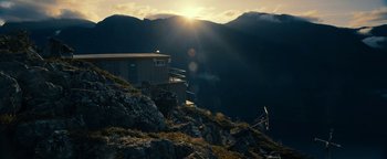 Movie still from “The Wave” (2015), directed by Roar Uthaug – The sun is setting over a mountain with a building; Extreme Wide shot, Low angle