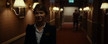 Movie still from “The Wave” (2015), directed by Roar Uthaug – A woman standing in a hotel hallway smiling for the camera; Medium shot, Over the shoulder angle