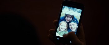Movie still from “The Wave” (2015), directed by Roar Uthaug – A person is holding a cell phone with a picture of a family on it; Extreme Close Up shot, Overhead angle