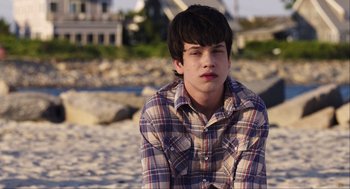 Movie still from “The Way Way Back” (2013), directed by Jim Rash – A young man sitting on the beach in a plaid shirt; Close Up shot, Over the shoulder angle