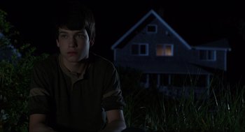 Movie still from “The Way Way Back” (2013), directed by Jim Rash – A young man sitting in the grass in front of a house at night; Medium shot, Over the shoulder angle