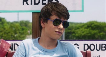 Movie still from “The Way Way Back” (2013), directed by Jim Rash – A young man wearing sunglasses sitting in front of a sign; Close Up shot, Over the shoulder angle