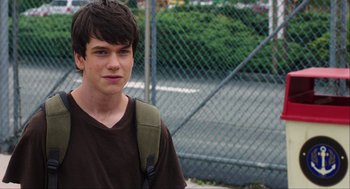Movie still from “The Way Way Back” (2013), directed by Jim Rash – A young man with a backpack standing in front of a chain link fence; Close Up shot, Over the shoulder angle