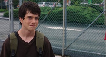 Movie still from “The Way Way Back” (2013), directed by Jim Rash – A young man with a backpack standing in front of a fence; Close Up shot, Over the shoulder angle