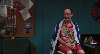Movie still from “The Way Way Back” (2013), directed by Jim Rash – A man sitting on a chair with a towel around his neck; Medium shot, Over the shoulder angle