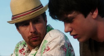 Movie still from “The Way Way Back” (2013), directed by Jim Rash – A man wearing a straw hat and a hawaiian shirt looks at another man; Close Up shot, Over the shoulder angle