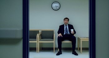 Movie still from “The Weather Man” (2005), directed by Gore Verbinski – A man in a suit sitting on a chair holding a coffee cup; Wide shot, Low angle