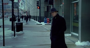 Movie still from “The Weather Man” (2005), directed by Gore Verbinski – An older man in a black coat and a black hat is walking down the street; Medium shot, Over the shoulder angle