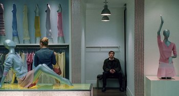 Movie still from “The Weather Man” (2005), directed by Gore Verbinski – A man sitting on a bench next to a woman in a store; Wide shot, Over the shoulder angle