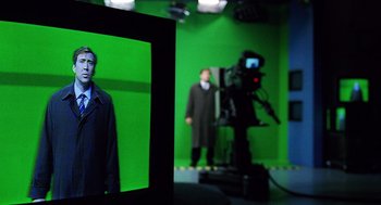 Movie still from “The Weather Man” (2005), directed by Gore Verbinski – A man in a suit and tie in front of a green screen; Medium shot, Over the shoulder angle