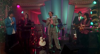 Movie still from “The Wedding Singer” (1998), directed by Frank Coraci – A man in a suit and tie singing into a microphone on a stage; Wide shot, Low angle