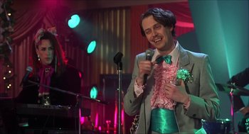 Movie still from “The Wedding Singer” (1998), directed by Frank Coraci – A man in a green suit holding a microphone; Medium shot, Low angle