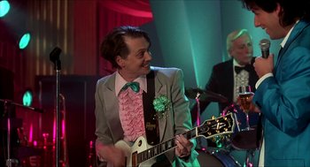 Movie still from “The Wedding Singer” (1998), directed by Frank Coraci – A man in a suit and tie playing a guitar; Medium shot, Low angle