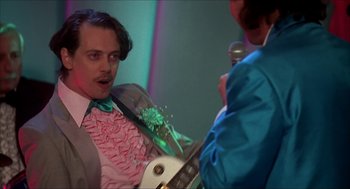 Movie still from “The Wedding Singer” (1998), directed by Frank Coraci – A man in a suit and tie holding an electric guitar; Medium shot, Low angle