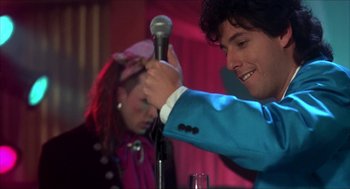 Movie still from “The Wedding Singer” (1998), directed by Frank Coraci – A man holding a microphone while a woman stands behind him; Close Up shot, Over the shoulder angle