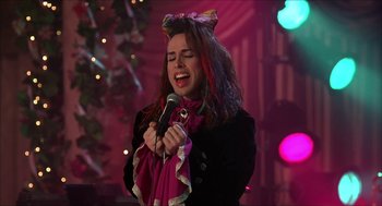 Movie still from “The Wedding Singer” (1998), directed by Frank Coraci – A woman in a black jacket is singing into a microphone; Medium shot, Over the shoulder angle