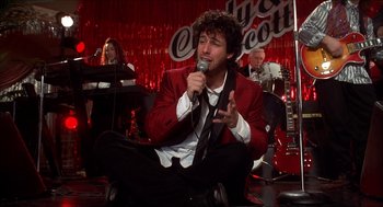 Movie still from “The Wedding Singer” (1998), directed by Frank Coraci – A man sitting on the ground while holding a microphone; Medium shot, High angle